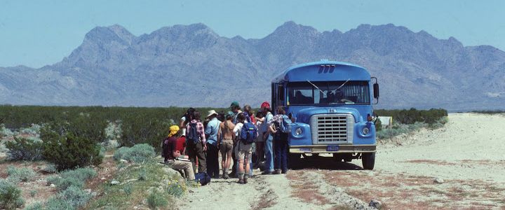 students exit big blue school bus in the mojave desert with the granit mountains ahead of them